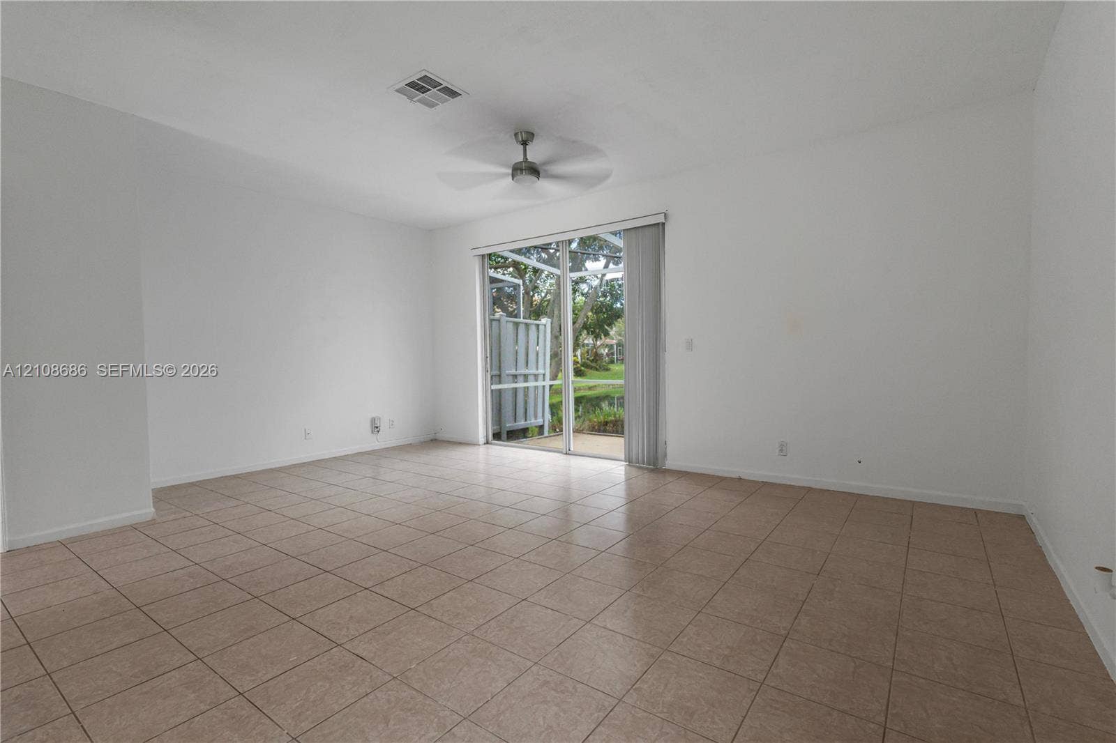 Interior space featuring neutral-toned tile flooring, a ceiling fan, and sliding glass doors that open to an outdoor screened enclosure