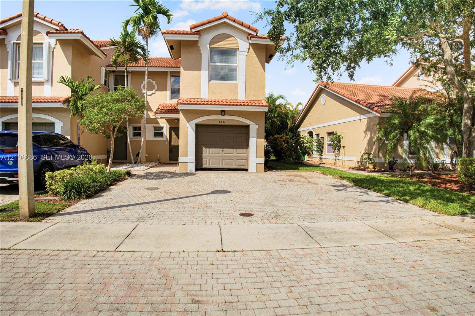 Stucco exterior with a tiled roof, attached garage, and paved driveway