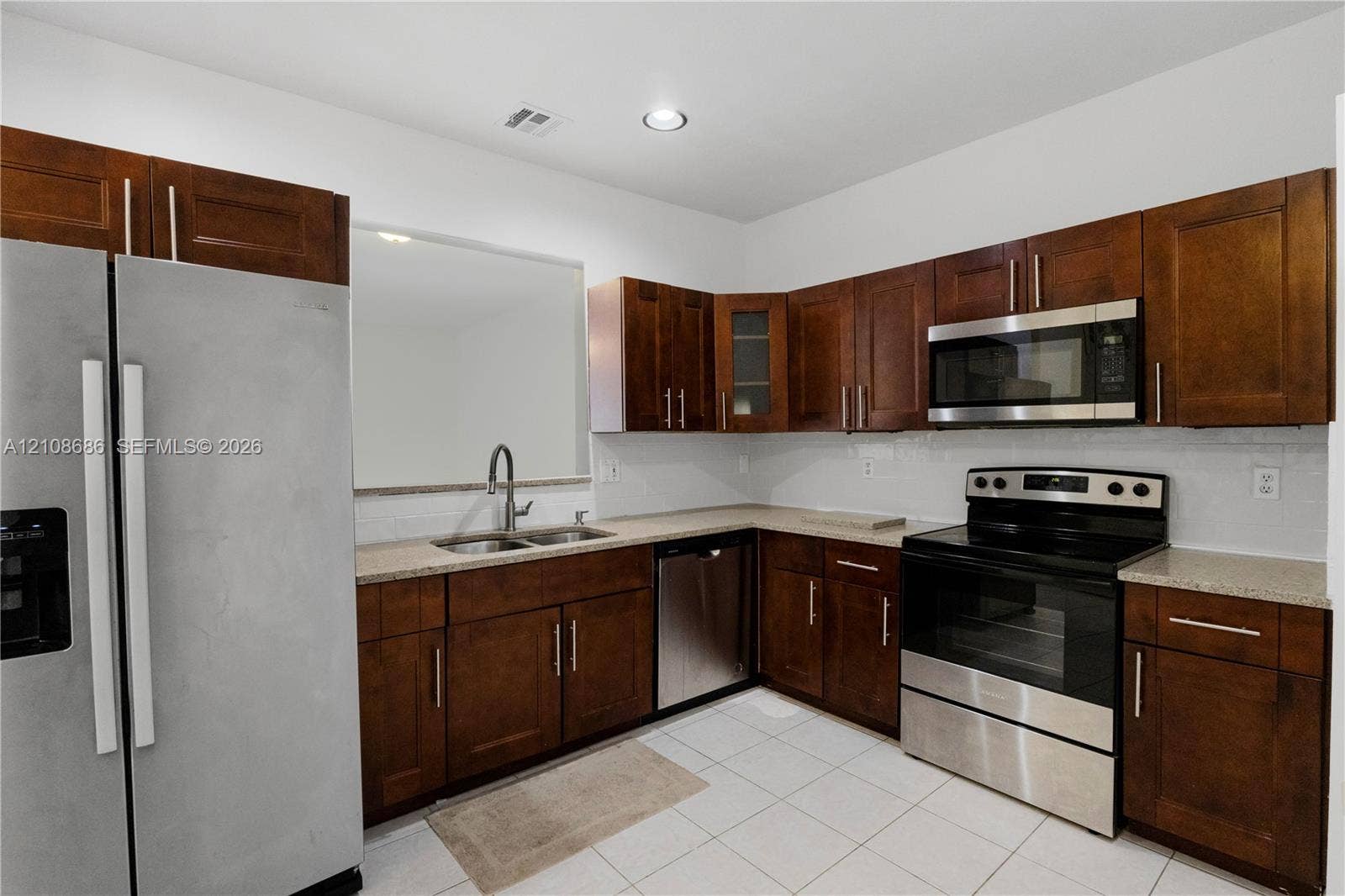 Kitchen featuring stained wood cabinetry, stone countertops, stainless steel appliances, and a double-basin stainless steel sink with a high-arch faucet