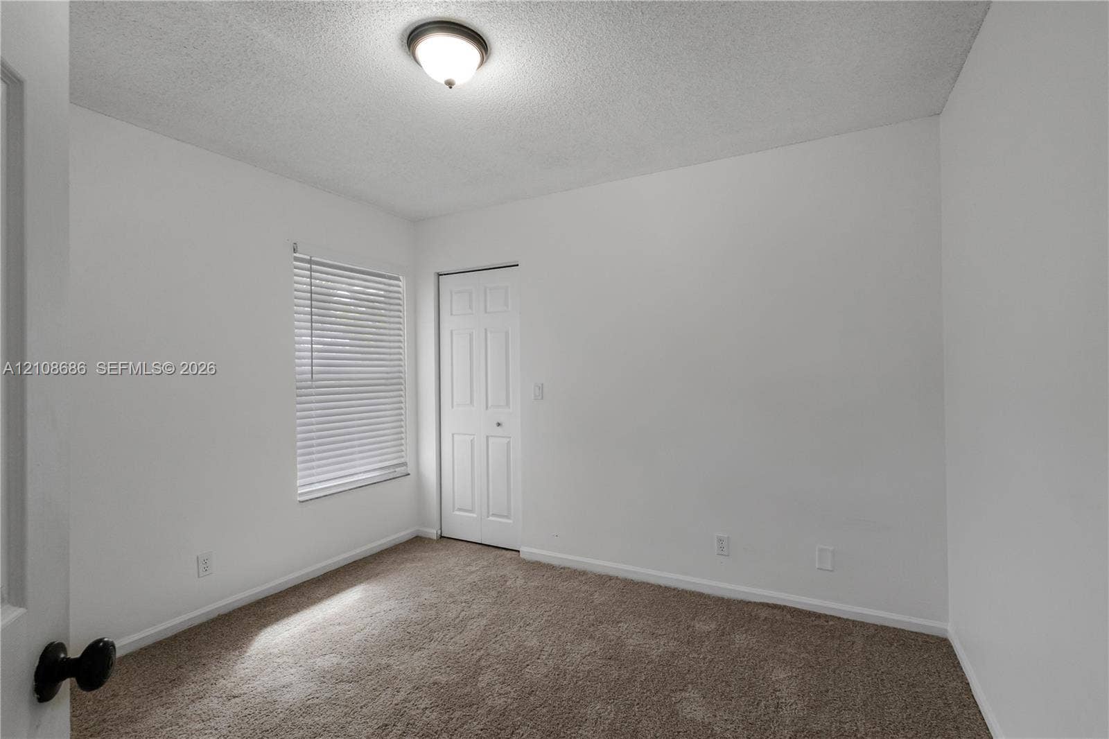 Neutral-toned wall-to-wall carpeting, window with integrated blinds, and multi-panel interior door