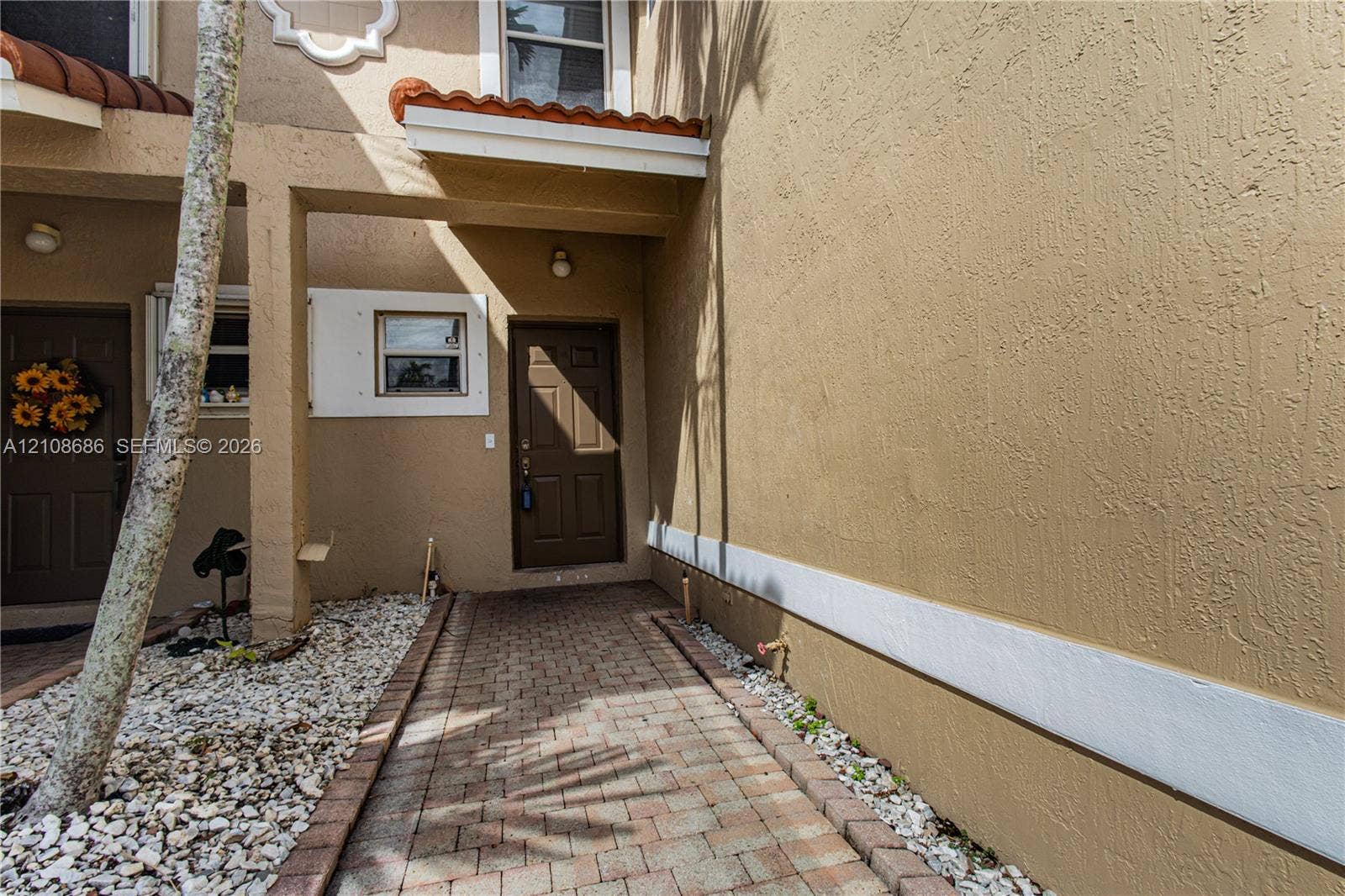 Stucco exterior featuring a brick-paver walkway, tile-capped roof accents, and a panelled entry door