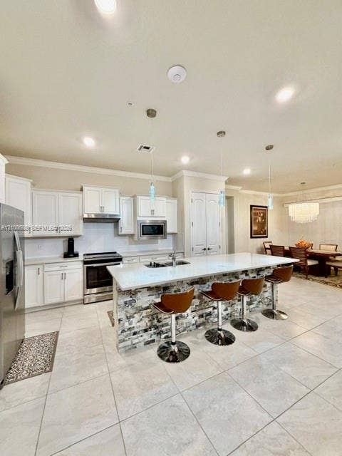 Kitchen featuring white cabinetry, stone-veneer island base, quartz countertops, stainless steel appliances, and large-format tile flooring