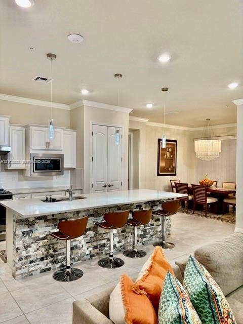 Kitchen featuring a stone-veneer island with a white quartz countertop, white cabinetry, stainless steel built-in microwave, three modern pendant lights, and tile flooring