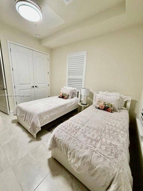 Room featuring neutral-toned tile flooring, tray ceiling with recessed lighting, double-door closet, and window with shutter blinds