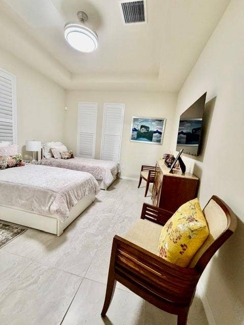 Tray ceiling featuring a central flush-mount light fixture, stone-finish tile flooring, and plantation shutters