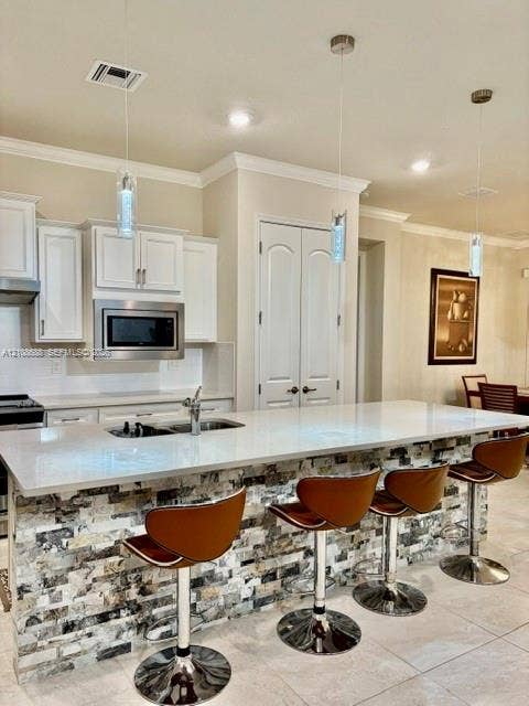 Kitchen featuring white cabinetry, solid surface countertops, a stone-veneer island facade, and triple pendant lighting