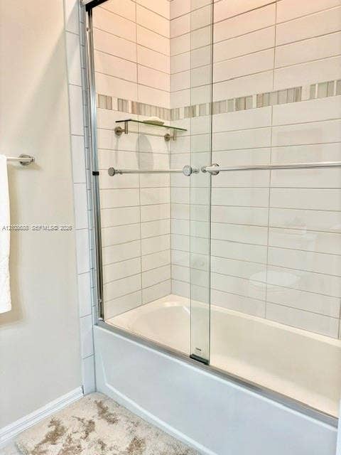 Bathtub enclosure featuring white horizontal subway-style wall tile, a glass sliding shower door with chrome hardware, an integrated glass corner shelf, and a decorative mosaic accent border