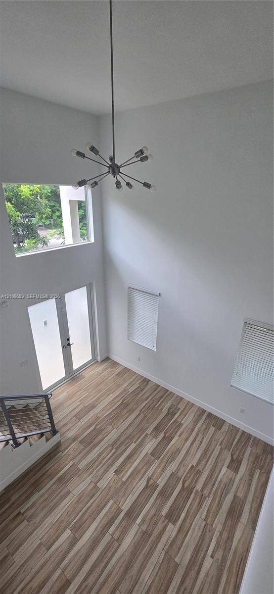Miami, Miami, FL 33133 Double-height ceiling featuring a contemporary sputnik-style chandelier, wood-finish tile flooring, double glass-paneled entry doors, and a staircase with metal horizontal railings