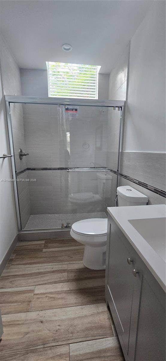 Miami, Miami, FL 33133 Walk-in shower with sliding glass door, tiled wall surround, skylight, wood-finish flooring, and vanity with solid surface countertop