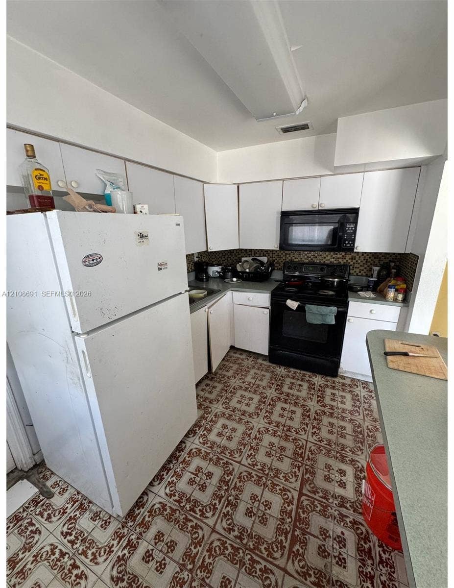 17210 NW 47th Avenue, Miami Gardens, FL 33055 Kitchen featuring white cabinetry, patterned tile flooring, an integrated microwave, and a black range