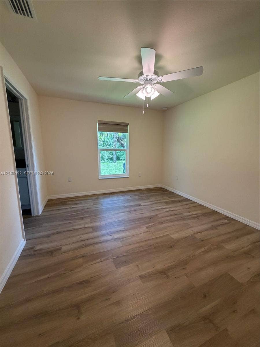 Interior room featuring wood-finish flooring, a neutral wall palette, a single-hung window with a roller shade, and a central ceiling fan with an integrated light fixture