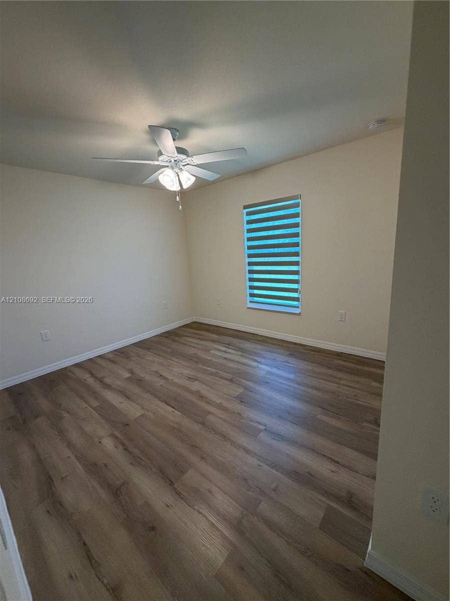 Room interior featuring wood-finish flooring, a ceiling fan with integrated lighting, and a window with horizontal shade treatment