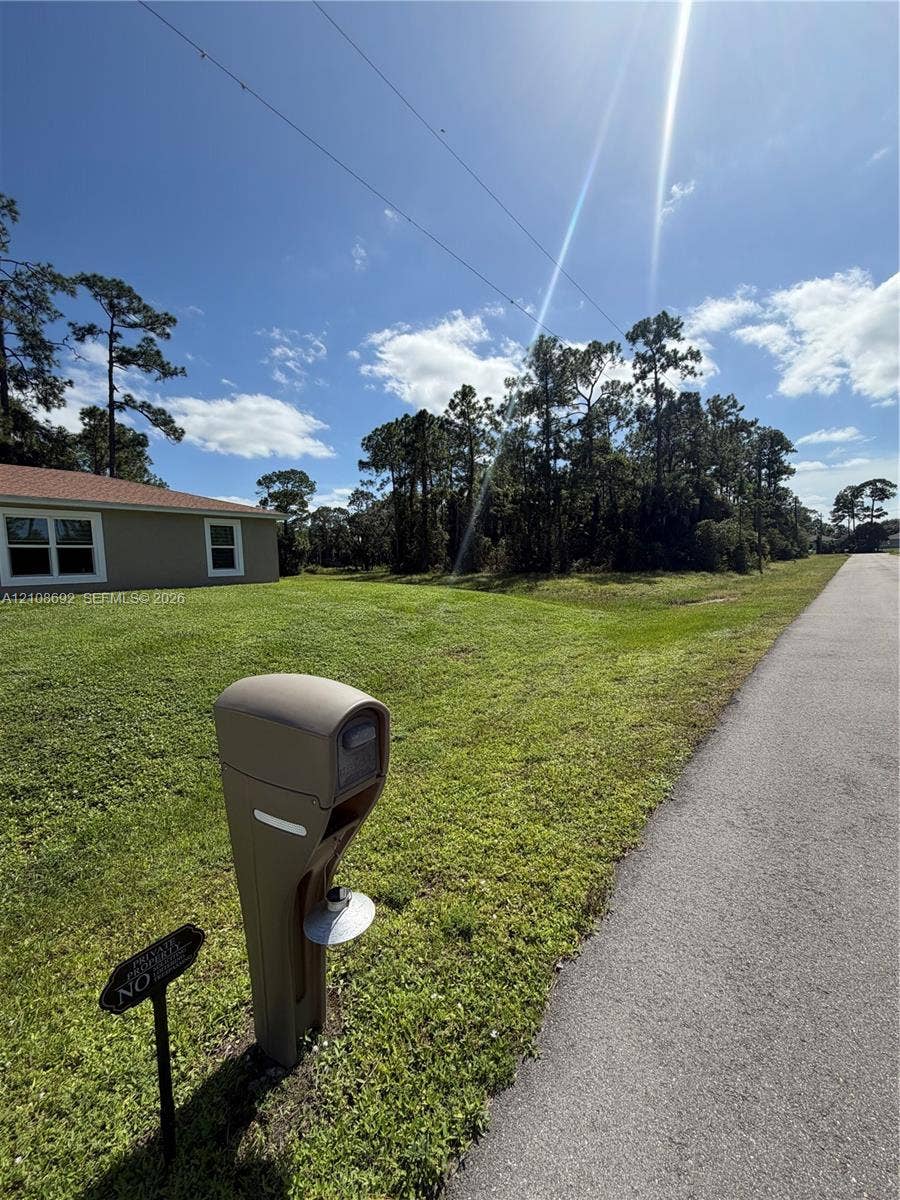 Expansive lot featuring a manicured lawn, mature trees, asphalt roadway access, and a neutral-toned exterior finish
