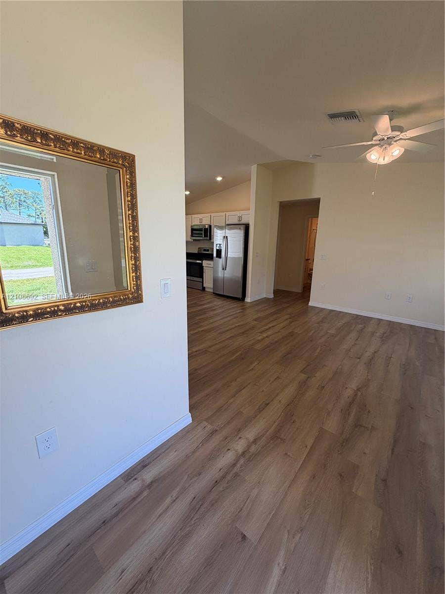 Wood-finish flooring, vaulted ceilings, ceiling fan with integrated lighting, and stainless steel kitchen appliances