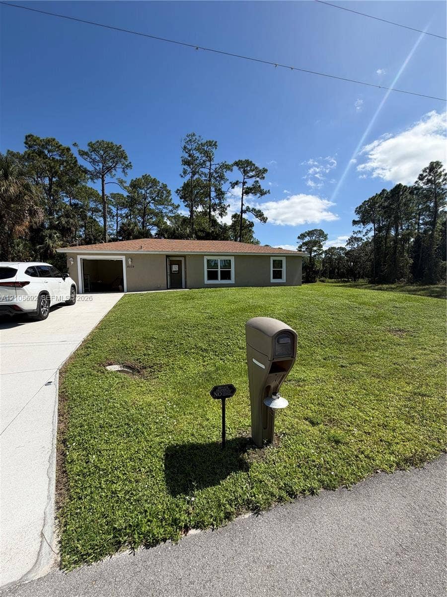 Single-story residence featuring a concrete driveway, attached garage, and expansive lawn with mature perimeter trees