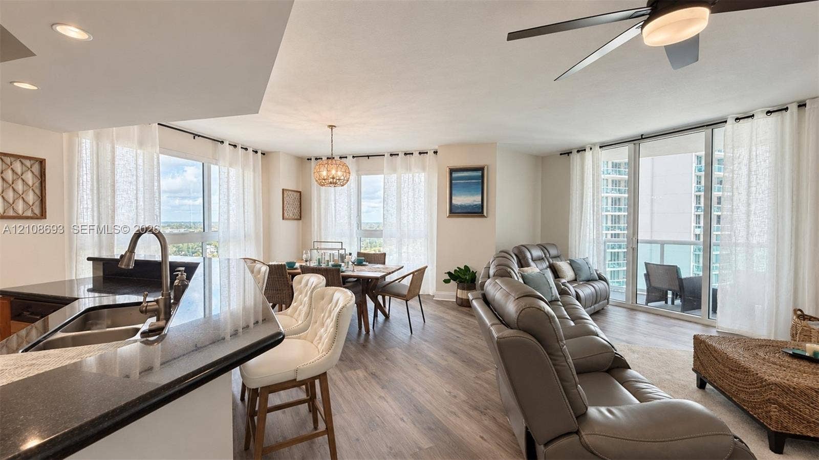 231 Riverside Drive, #1210, Daytona Beach, Daytona Beach, FL 32117 Open-concept interior featuring wood-finish flooring, a kitchen peninsula with a stone countertop, an integrated stainless steel dual-basin sink, floor-to-ceiling glass panel doors, and a modern drum-style pendant light