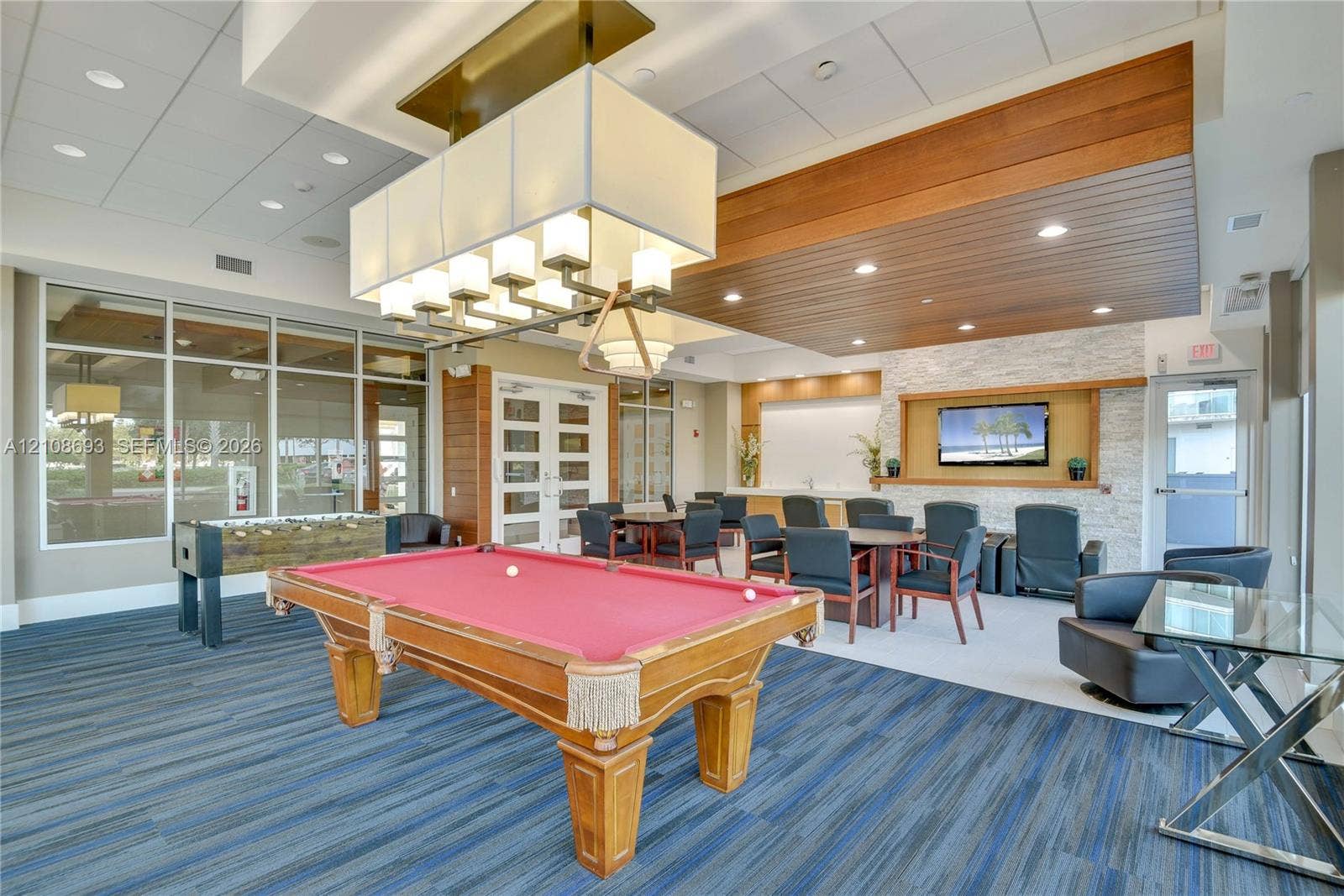 231 Riverside Drive, #1210, Daytona Beach, Daytona Beach, FL 32117 Recreation space featuring a coffered ceiling with integrated wood paneling, stone accent wall, large-scale box chandelier, and expansive floor-to-ceiling windows