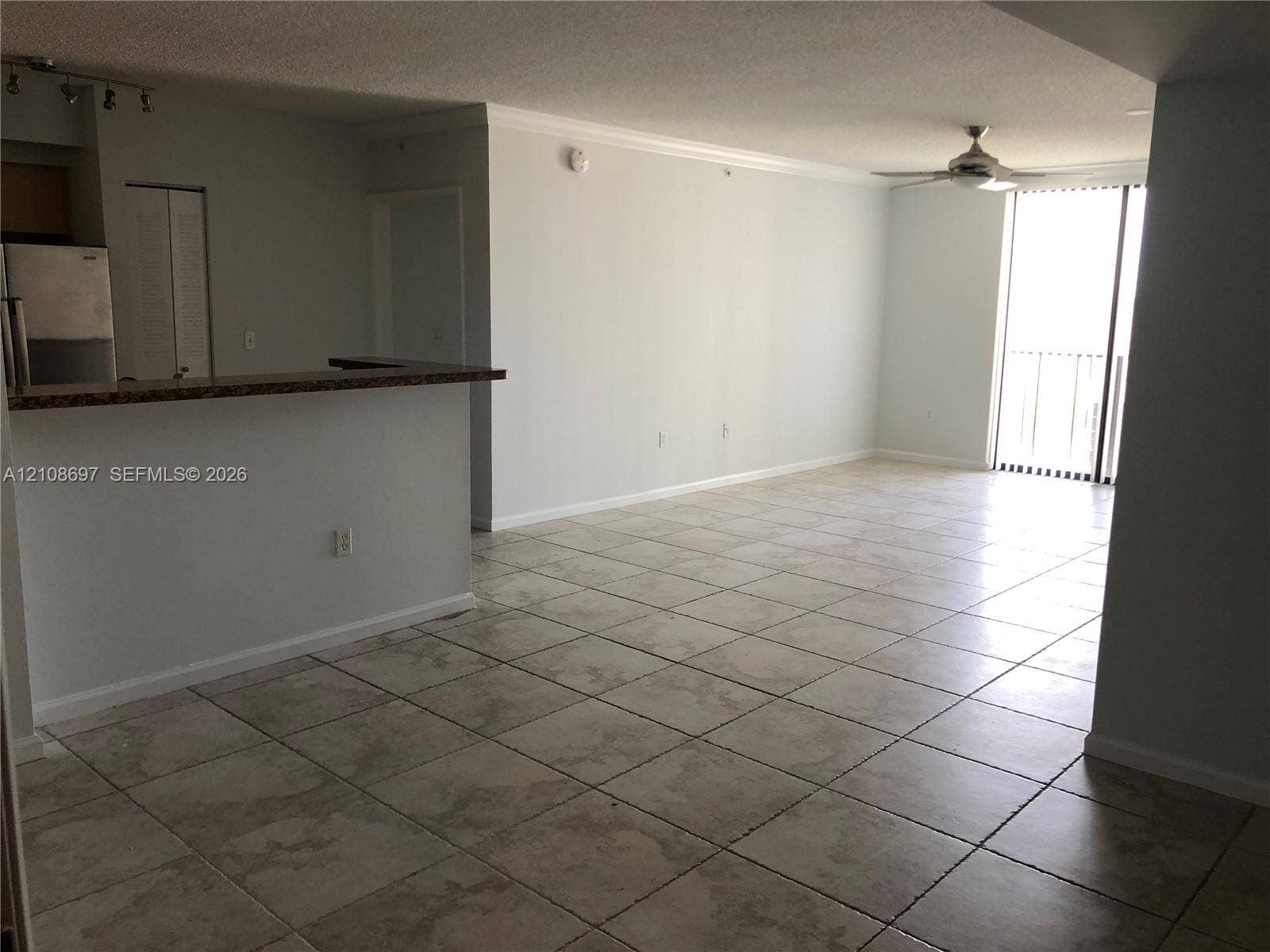 Open floor plan featuring tile flooring, a kitchen pass-through counter, ceiling fan, and sliding glass door access to a balcony