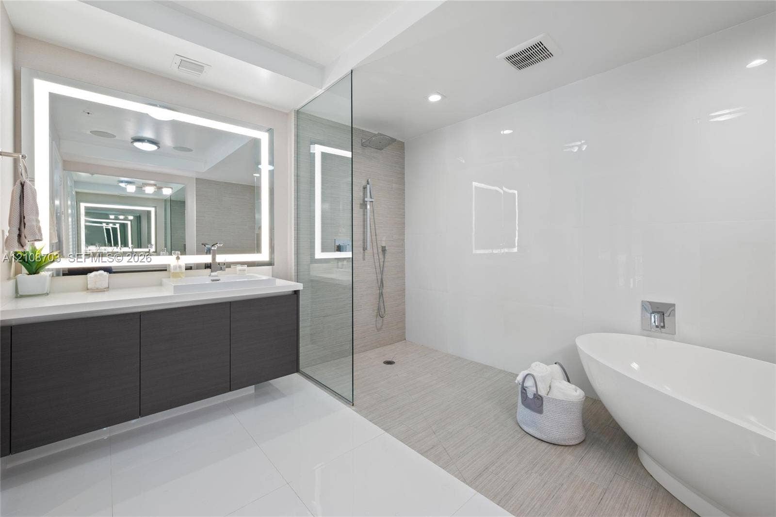 300 Sunny Isles Boulevard, #4-1501, Sunny Isles Beach, Sunny Isles Beach, FL 33160 Floating vanity with rectangular vessel sink, frameless glass-enclosed shower, wall-mounted shower fixture, backlit vanity mirror, and freestanding soaking tub