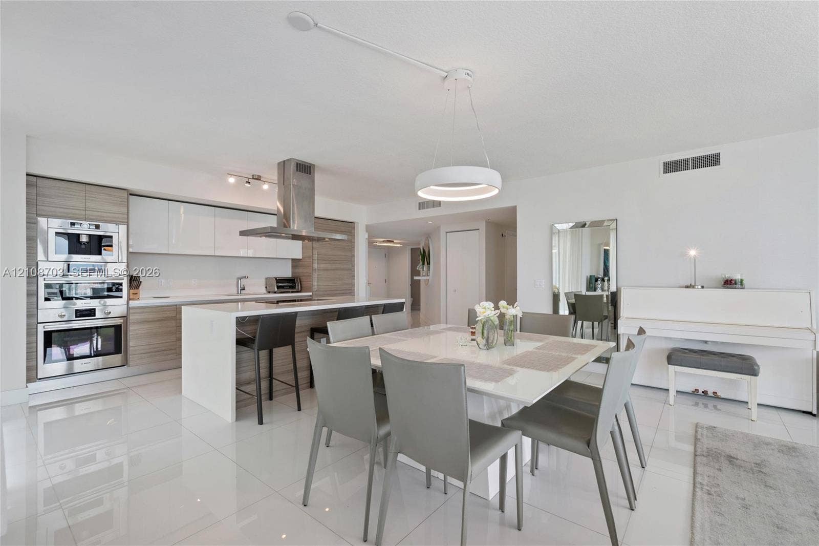 300 Sunny Isles Boulevard, #4-1501, Sunny Isles Beach, Sunny Isles Beach, FL 33160 Contemporary kitchen featuring high-gloss cabinetry, stainless steel built-in double ovens, a central island with a waterfall-edge countertop, a stainless steel chimney range hood, and white tile flooring