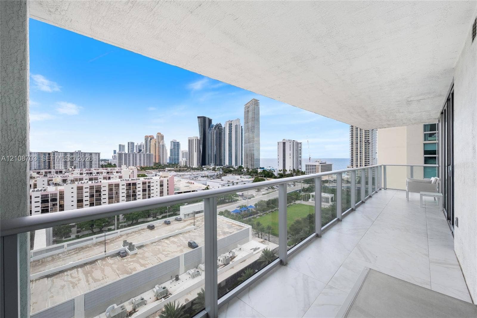 300 Sunny Isles Boulevard, #4-1501, Sunny Isles Beach, Sunny Isles Beach, FL 33160 Private covered balcony featuring large-format stone-finish flooring and a glass panel railing overlooking the urban skyline