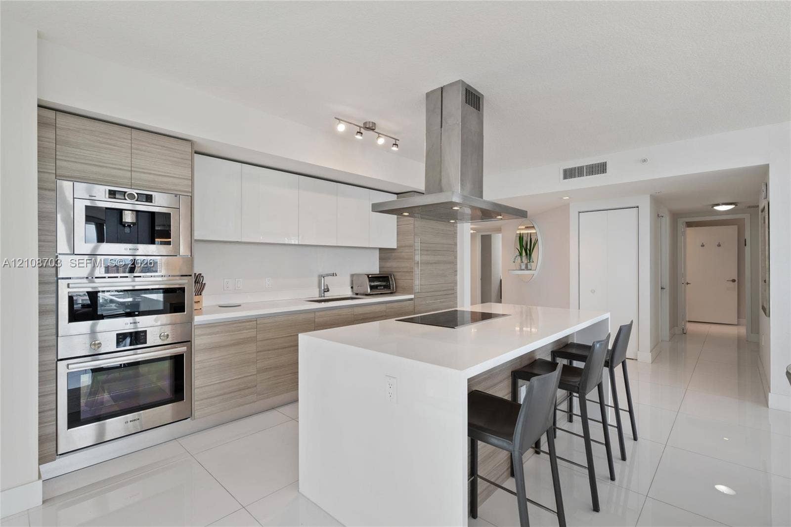 300 Sunny Isles Boulevard, #4-1501, Sunny Isles Beach, Sunny Isles Beach, FL 33160 Kitchen featuring a central island with a solid-surface countertop, high-gloss white and wood-finish cabinetry, built-in stainless steel appliances, and a ceiling-mounted stainless steel range hood