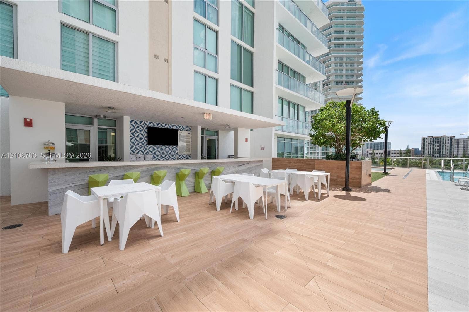 300 Sunny Isles Boulevard, #4-1501, Sunny Isles Beach, Sunny Isles Beach, FL 33160 Outdoor kitchen area featuring a stone-finish bar counter, decorative patterned backsplash, wood-finish tile flooring, and integrated wall-mounted television