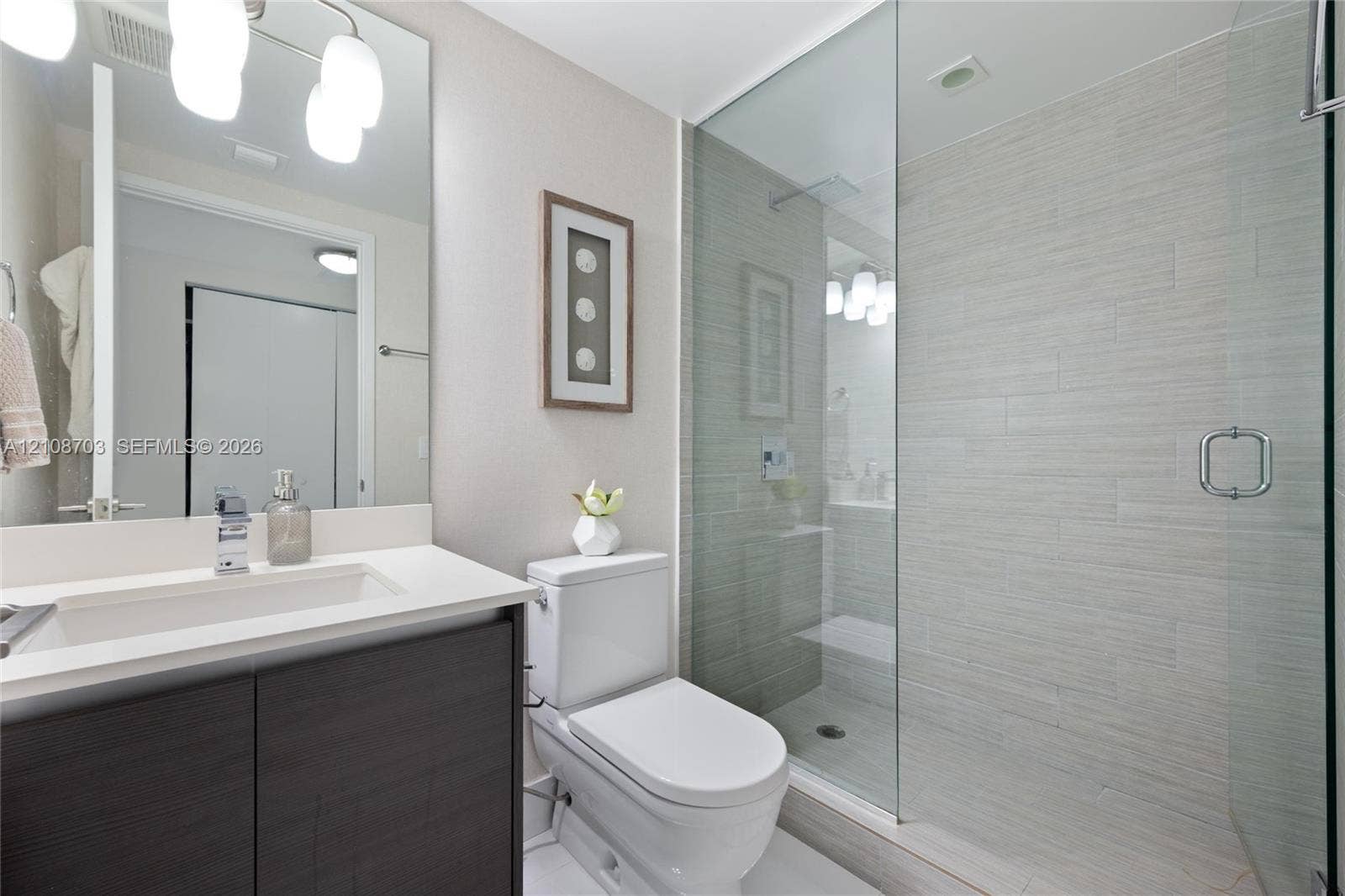 300 Sunny Isles Boulevard, #4-1501, Sunny Isles Beach, Sunny Isles Beach, FL 33160 Bathroom featuring a dark wood-finish vanity with a white countertop, integrated sink, large wall-mounted mirror, and walk-in shower with floor-to-ceiling tile and a frameless glass door