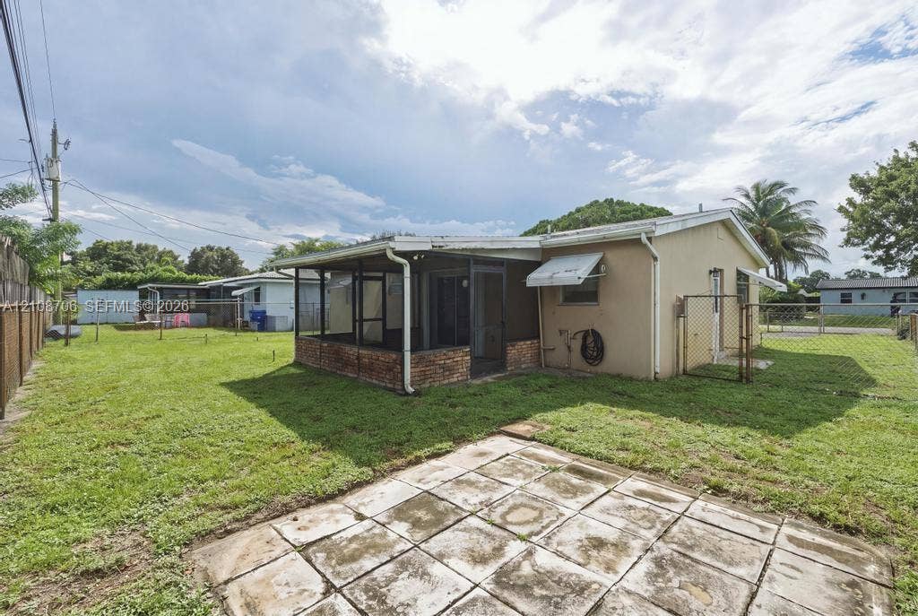 531 N 70th Way, Hollywood, FL 33024 Exterior featuring a screened-in porch with a brick base, concrete paver patio, chain-link perimeter fencing, and an expansive lawn