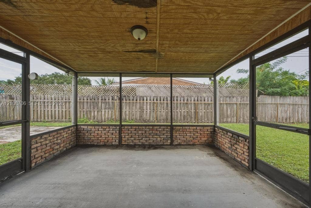 531 N 70th Way, Hollywood, FL 33024 Screened-in porch featuring exposed brick wall segments, concrete flooring, wood-paneled ceiling, and two metal-frame screen doors