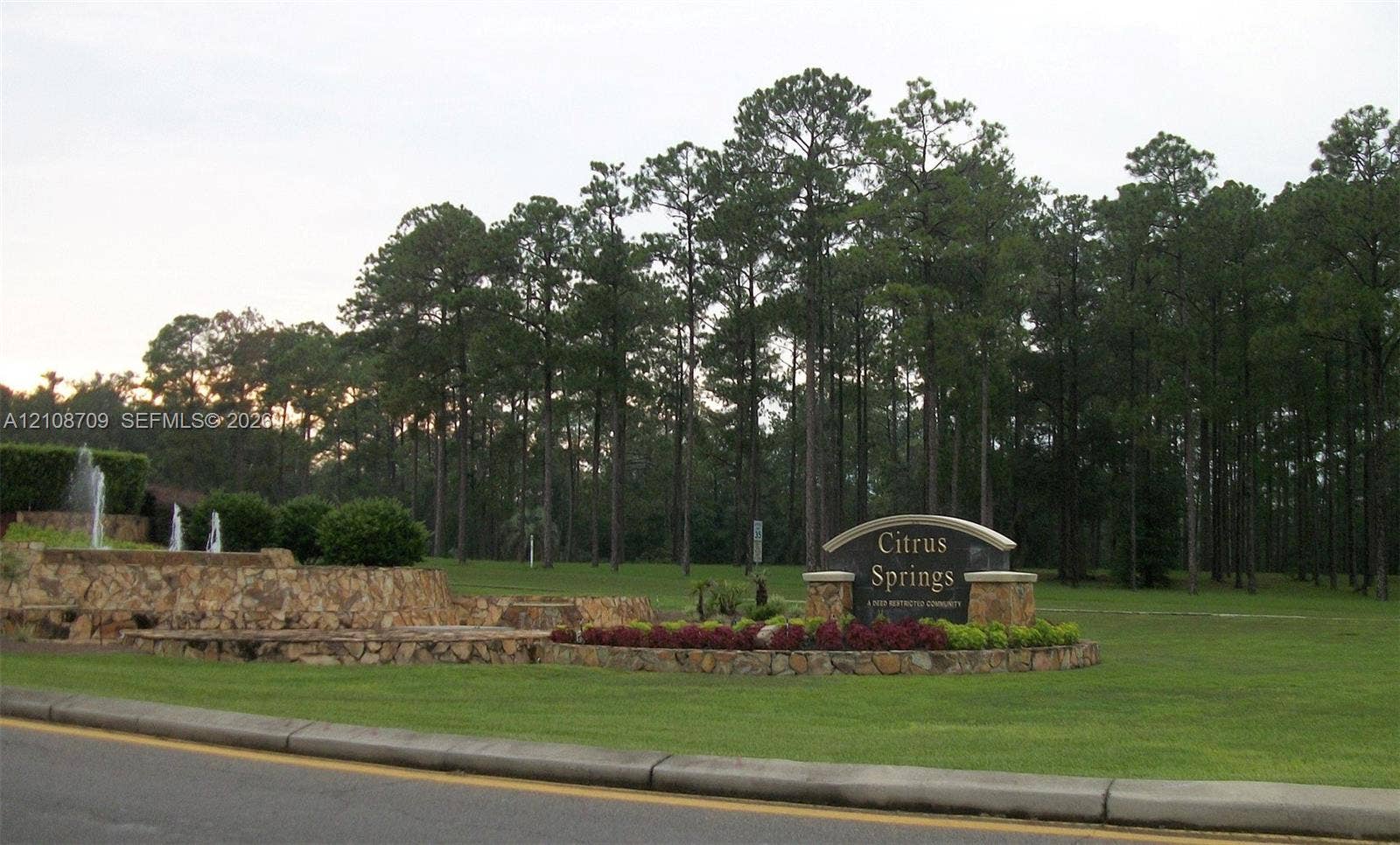 684 E Noah Lane, Citrus Springs, Citrus Springs, FL 34434 Community entrance featuring stone-veneer retaining walls, tiered landscaping, a multi-tiered fountain, and established pine forest surroundings