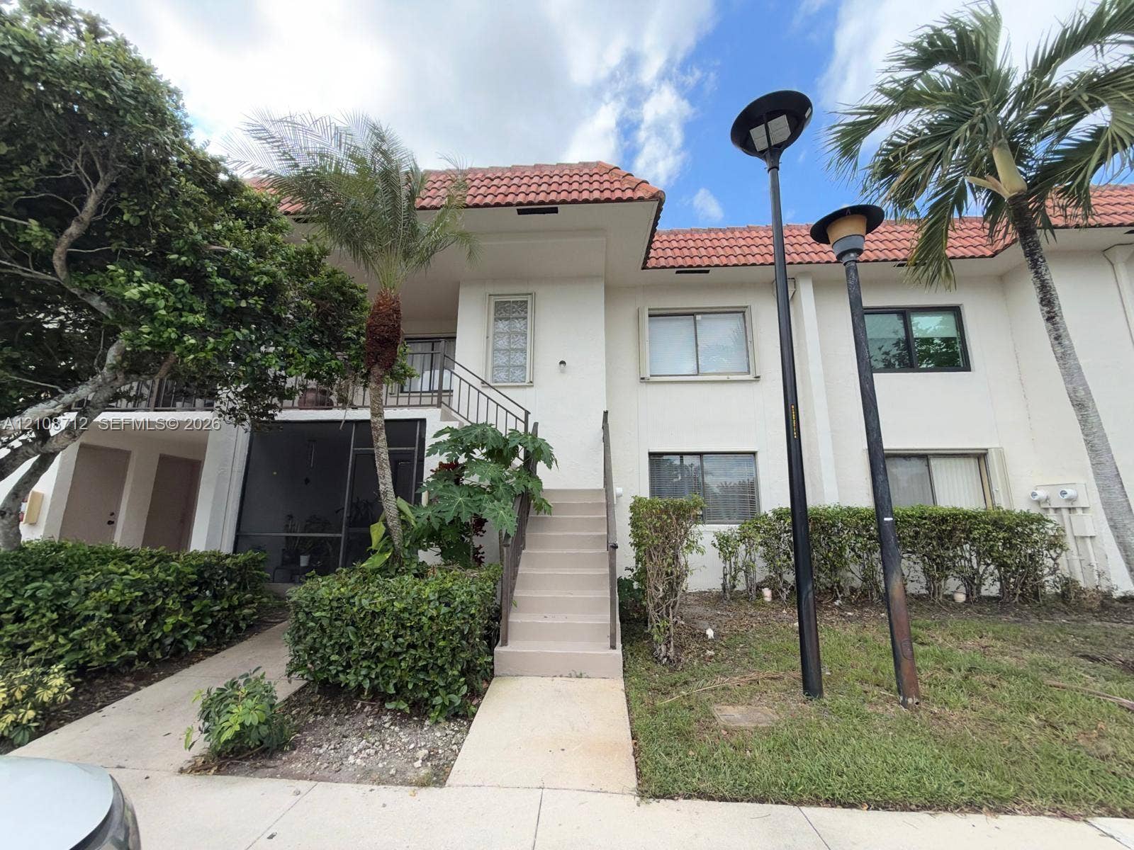 379 Lakeview Drive, #205, Weston, Weston, FL 33326 Two-story exterior featuring a terracotta tile roof, white stucco facade, screened-in entry, and a concrete staircase with metal handrails