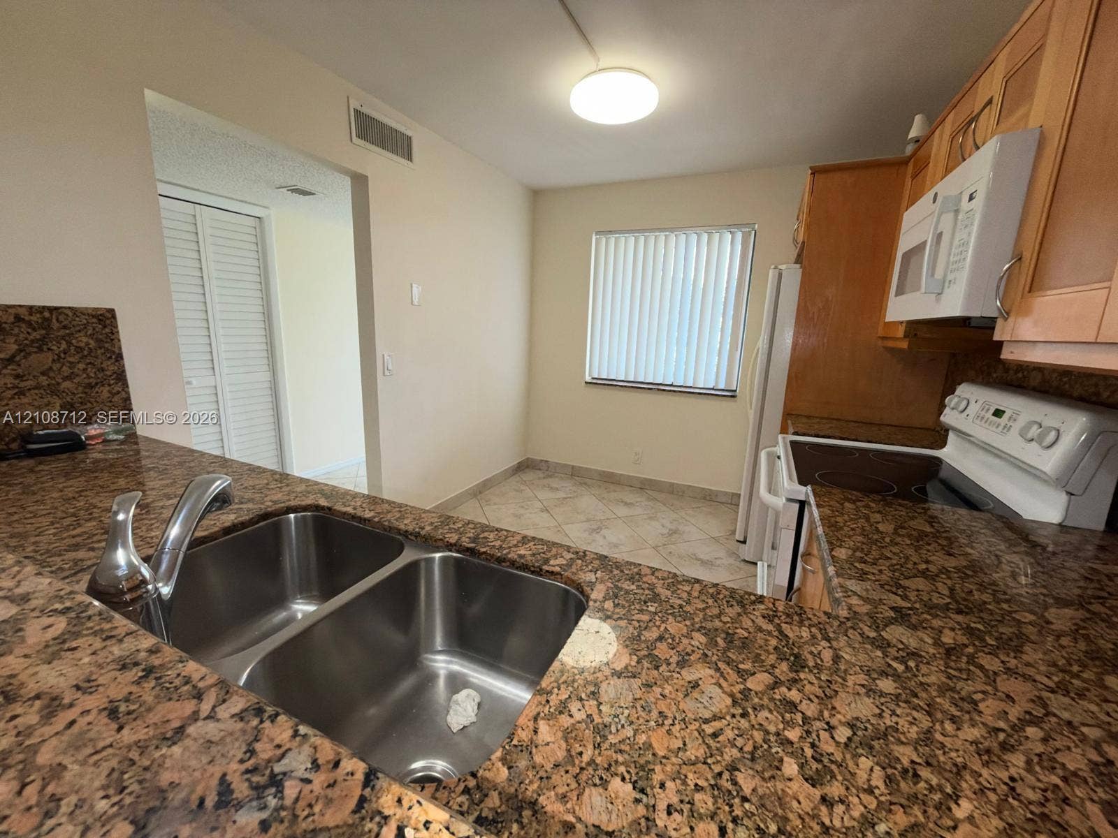 379 Lakeview Drive, #205, Weston, Weston, FL 33326 Kitchen featuring stone countertops, dual-basin stainless steel sink, light wood-finish cabinetry, tile flooring, and integrated microwave