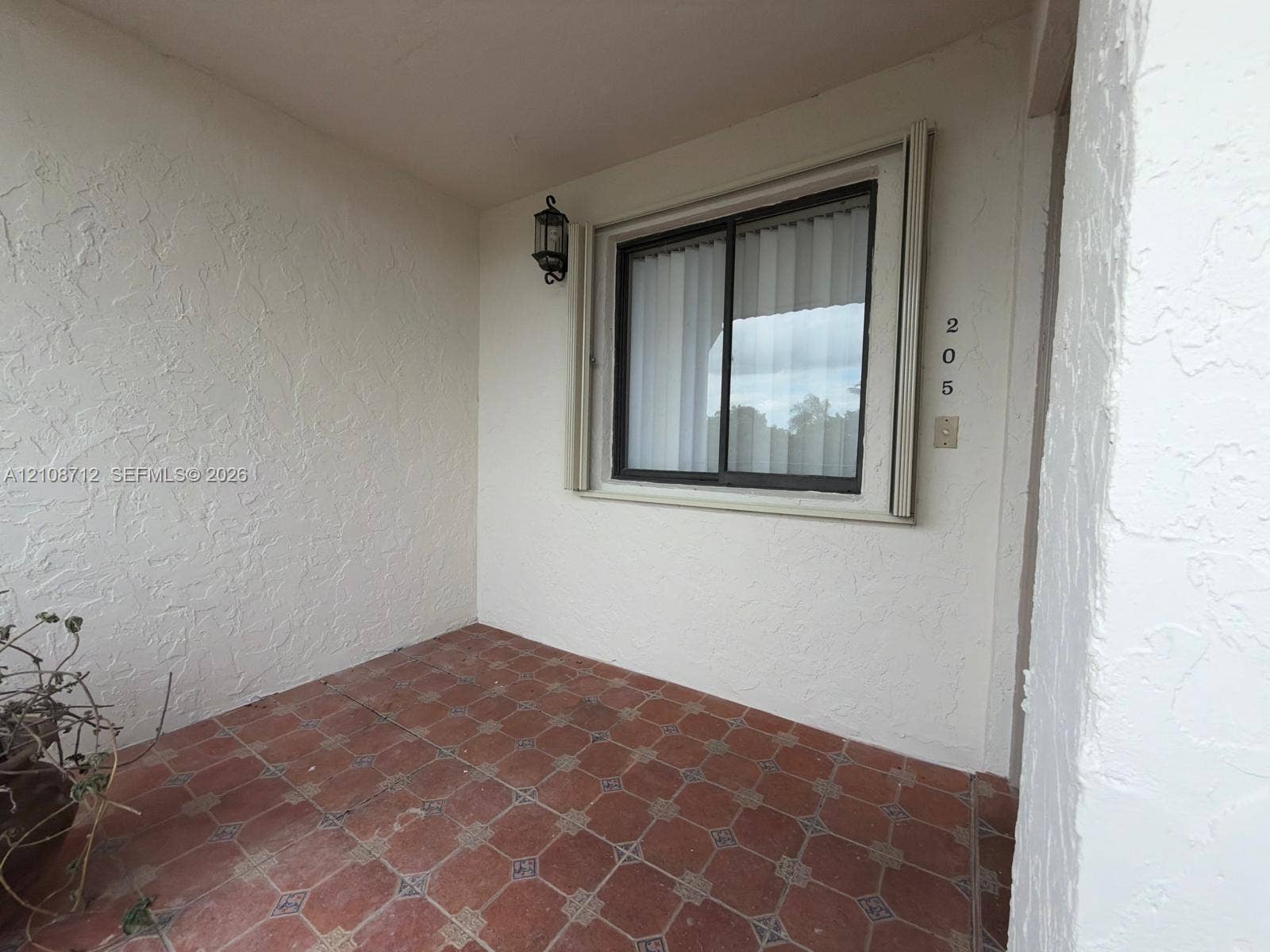 379 Lakeview Drive, #205, Weston, Weston, FL 33326 Covered entryway featuring terra cotta tile flooring, stucco wall finish, wall-mounted lantern lighting, and a window with a metal frame