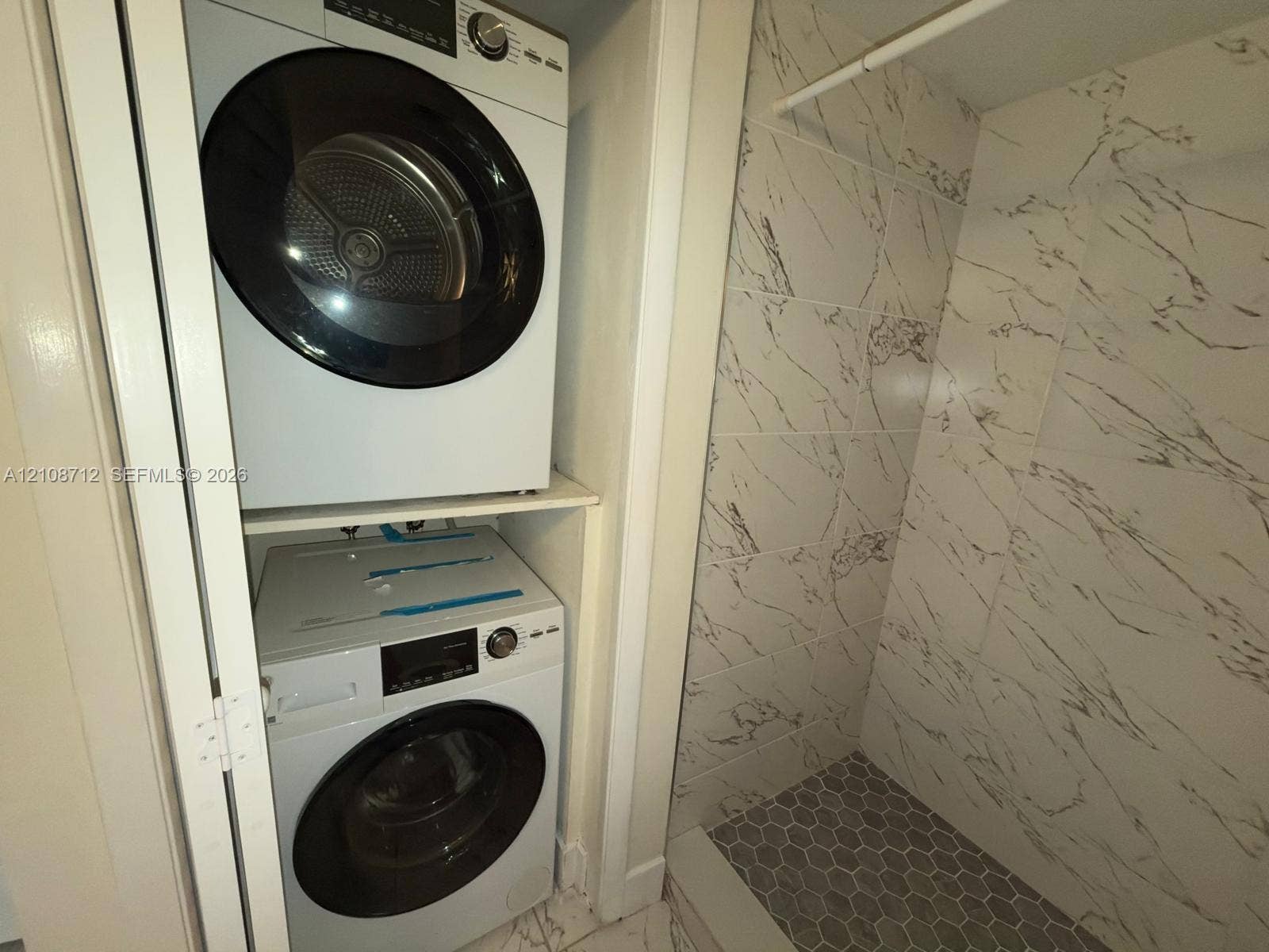 379 Lakeview Drive, #205, Weston, Weston, FL 33326 Laundry closet featuring stacked front-load appliances, large-format veined wall tile, built-in hanging rod, and hexagonal floor tiling