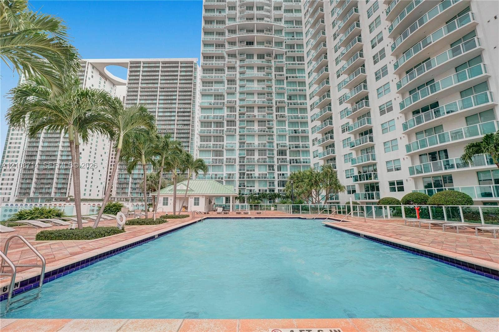 41 SE 5th Street, #317, Miami, Miami, FL 33131 Swimming pool featuring tile edging, paved decking, and integrated metal handrails, set amidst palm trees and high-rise structures