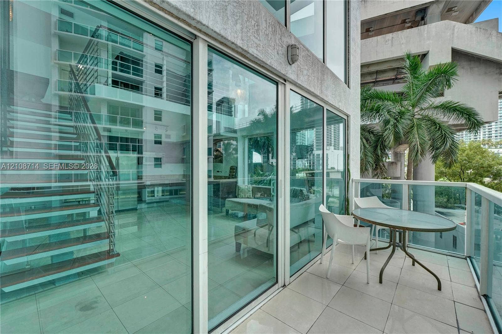 41 SE 5th Street, #317, Miami, Miami, FL 33131 Private balcony featuring tile flooring and a glass-paneled railing, floor-to-ceiling glass wall, and interior staircase with wood-finish treads and metallic railing