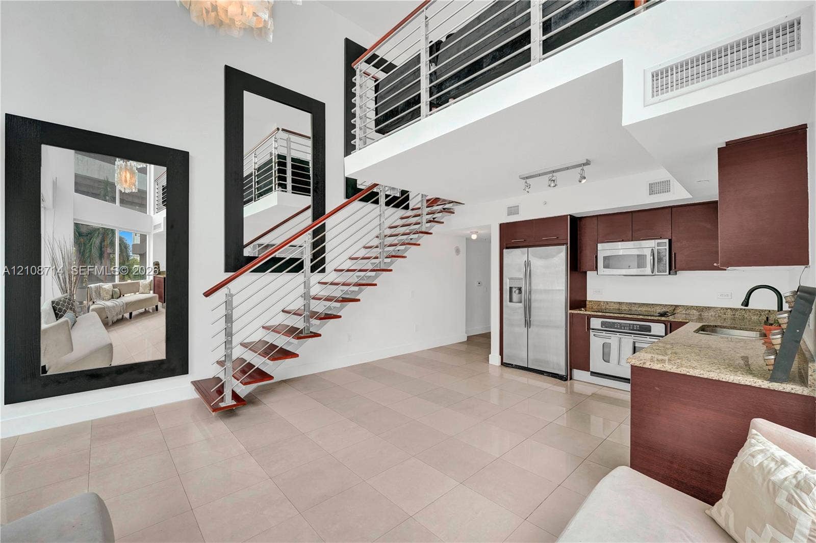 41 SE 5th Street, #317, Miami, Miami, FL 33131 Double-height living area featuring an open staircase with wood treads and horizontal metal railings, tile flooring, built-in cabinetry, and integrated stainless steel appliances