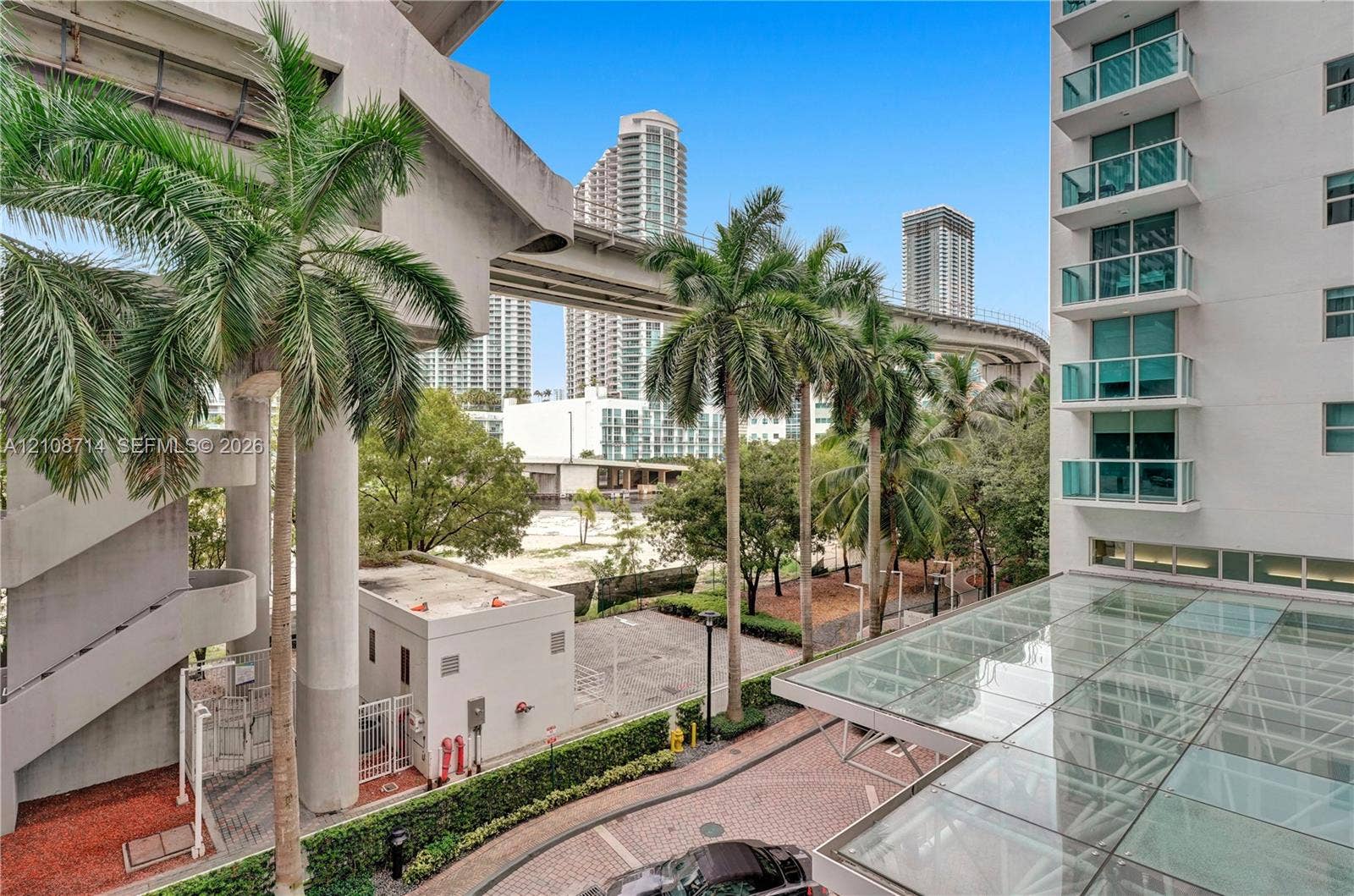 41 SE 5th Street, #317, Miami, Miami, FL 33131 High-rise building with glass-paneled balconies and a glass-covered entryway featuring patterned paver driveway and mature palm landscaping