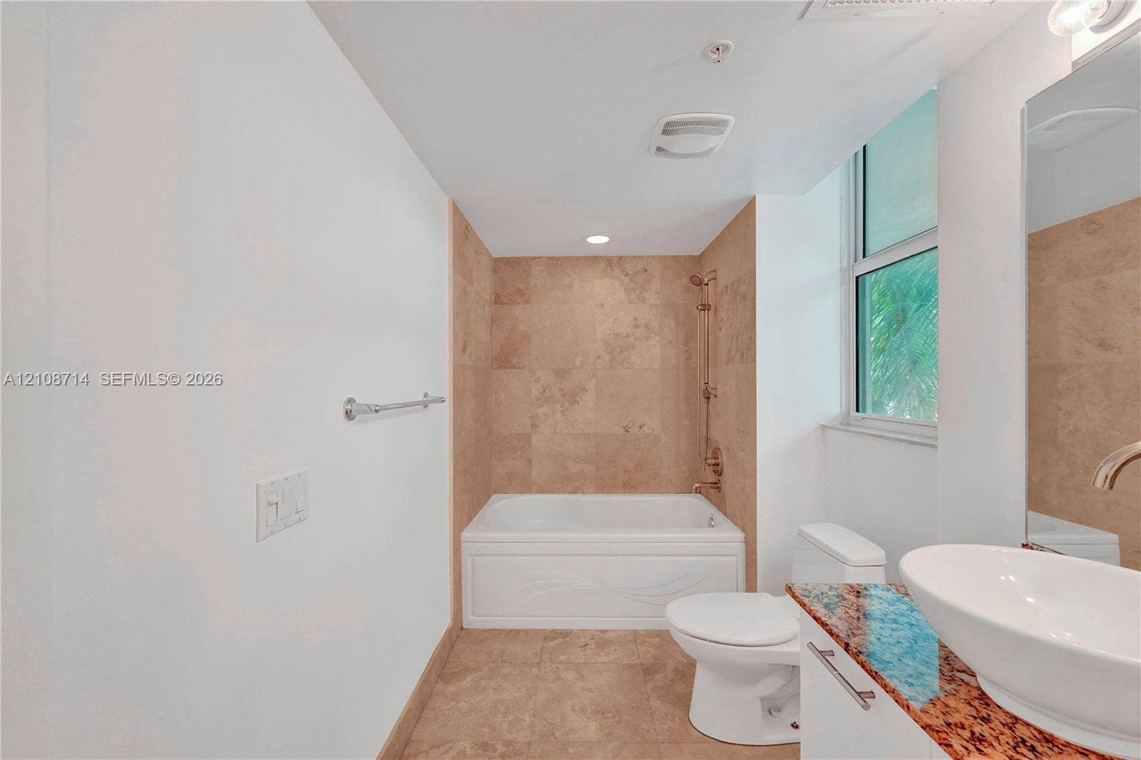 41 SE 5th Street, #317, Miami, Miami, FL 33131 Bathroom featuring a white soaking tub with a tiled surround, stone-finish vanity countertop, vessel sink, and large wall-mounted mirror