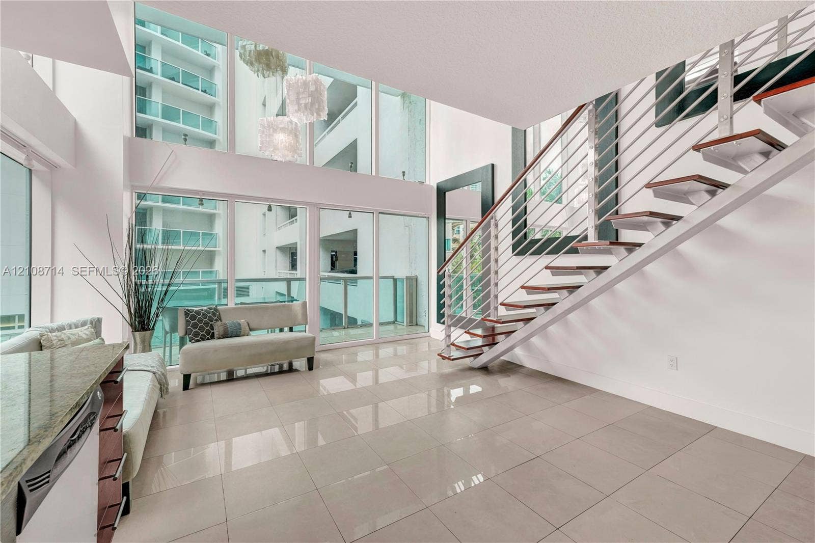 41 SE 5th Street, #317, Miami, Miami, FL 33131 Double-height floor-to-ceiling windows, open-riser staircase with horizontal cable railing, neutral large-format tile flooring, and built-in stone-surface kitchen cabinetry
