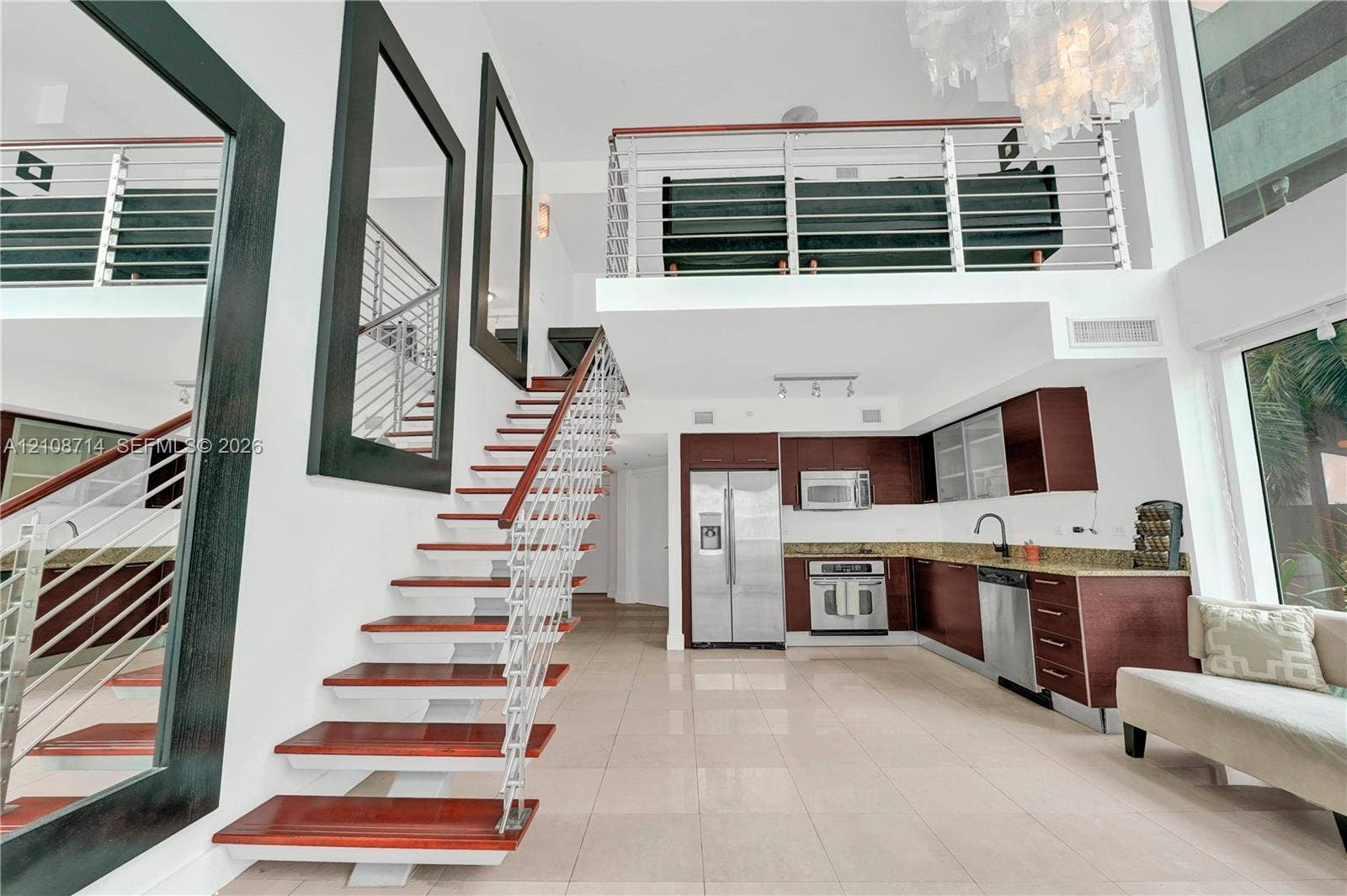 41 SE 5th Street, #317, Miami, Miami, FL 33131 Open-concept interior featuring high ceilings, wood-tread staircase with cable railing, lofted level, tile flooring, and kitchen cabinetry with stainless steel appliances