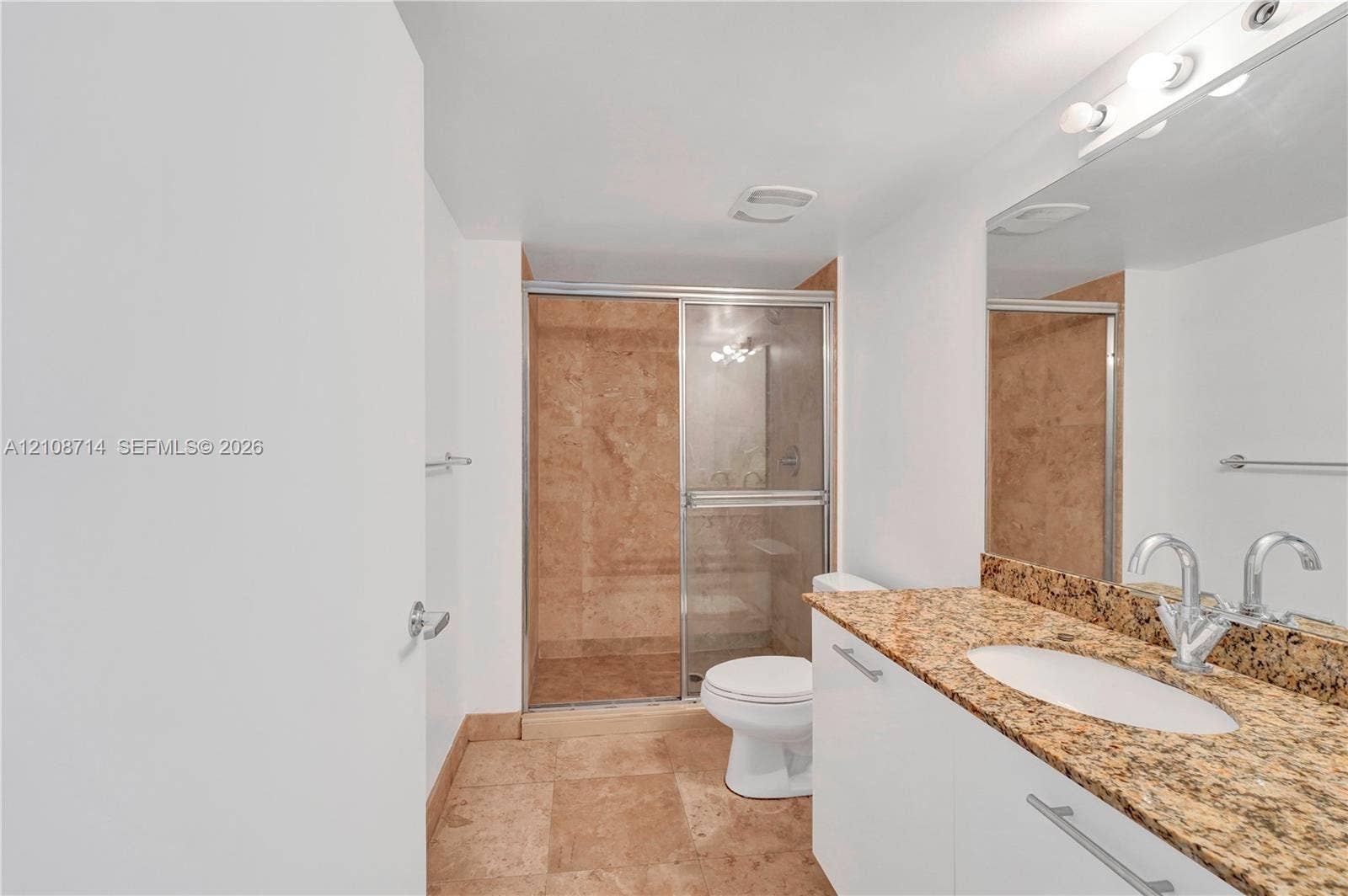 41 SE 5th Street, #317, Miami, Miami, FL 33131 Bathroom featuring stone-finish floor tiling, a stone-topped vanity with an oval undermount sink, a large wall-mounted mirror, and a walk-in shower with stone tile surround and sliding glass doors