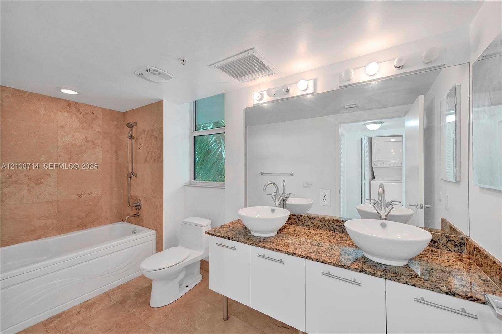 41 SE 5th Street, #317, Miami, Miami, FL 33131 Bathroom featuring a floating vanity with dual vessel sinks, stone-finish countertops, tiled shower surround with a handheld showerhead, and a full-width wall mirror