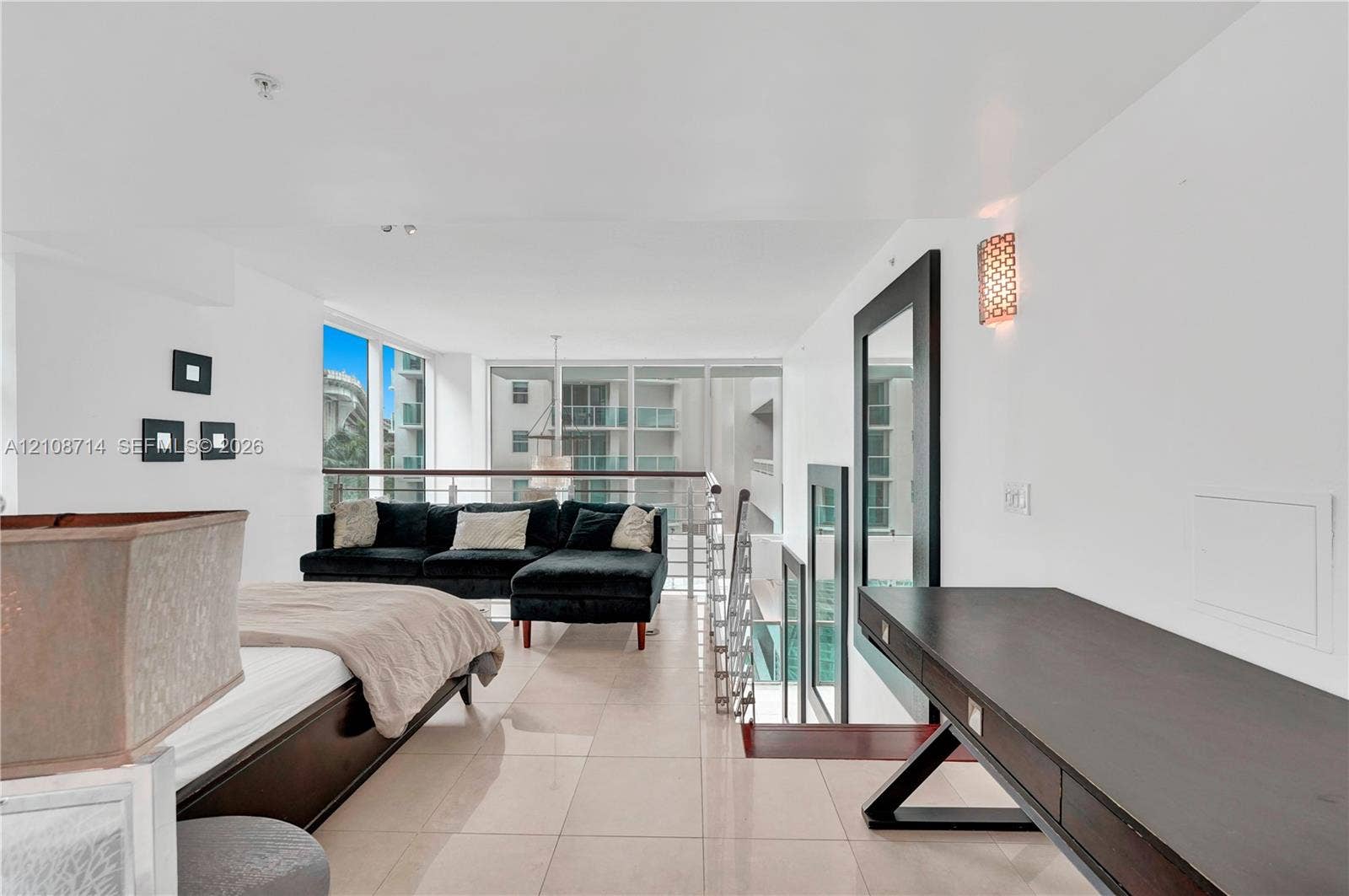 41 SE 5th Street, #317, Miami, Miami, FL 33131 Open-concept loft area featuring large-format tile flooring, a built-in dark wood desk, floor-to-ceiling windows, and a metal-railing staircase