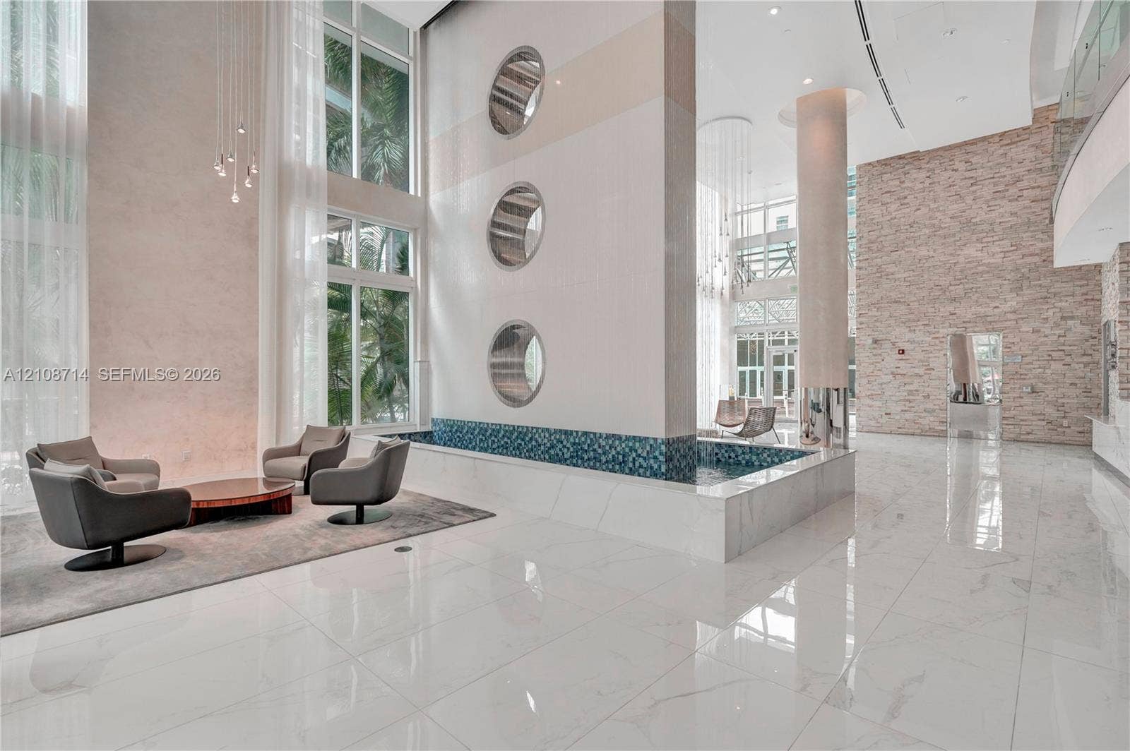 41 SE 5th Street, #317, Miami, Miami, FL 33131 Double-height ceilings featuring floor-to-ceiling windows, polished large-format tile flooring, a decorative indoor water feature with mosaic tile accents, circular wall portals, and textured stone wall cladding