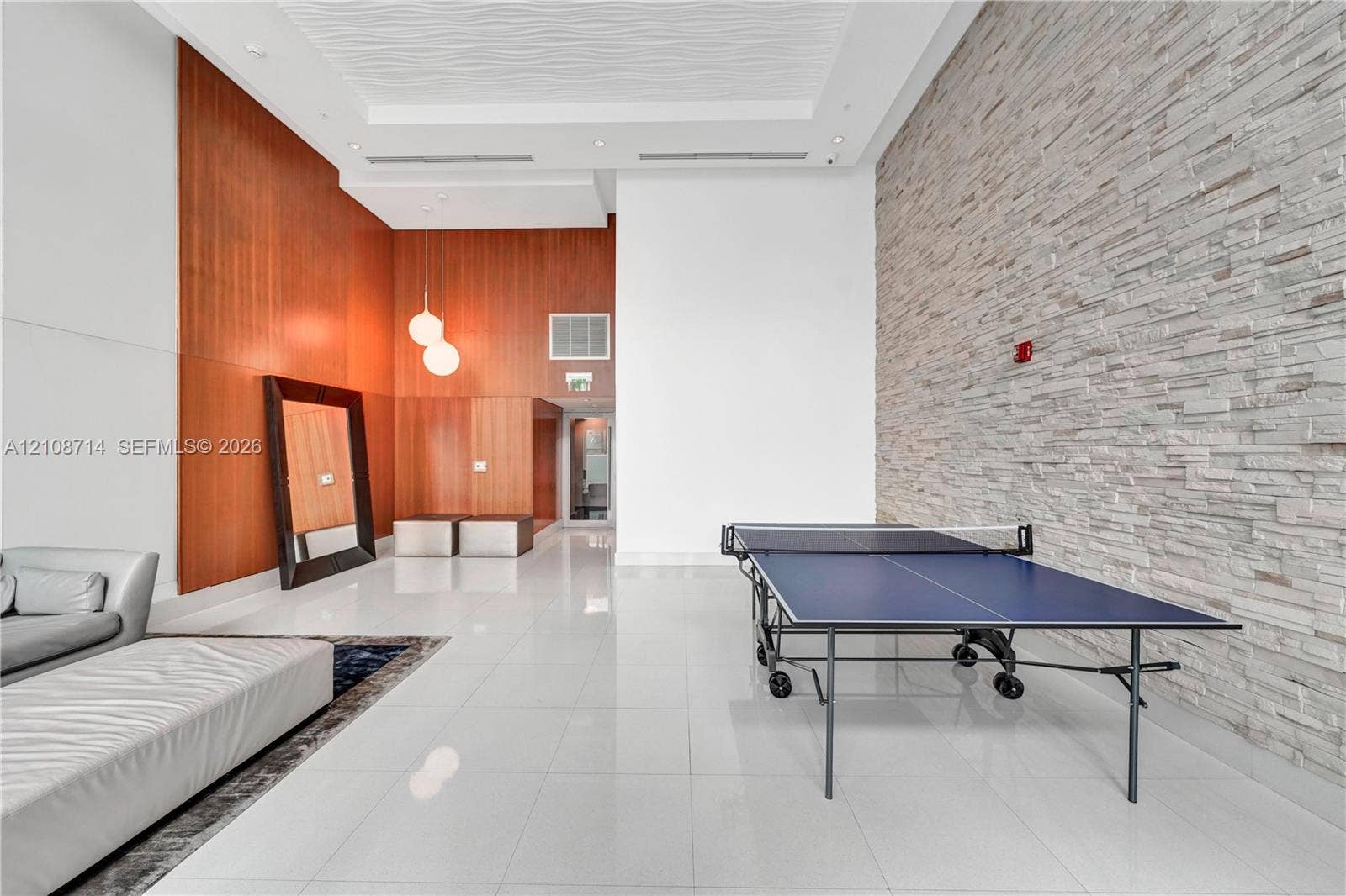 41 SE 5th Street, #317, Miami, Miami, FL 33131 High-ceiling interior featuring smooth wood paneling, floor-to-ceiling textured stone accent wall, glossy large-format tile flooring, recessed lighting, and modern globe pendant fixtures