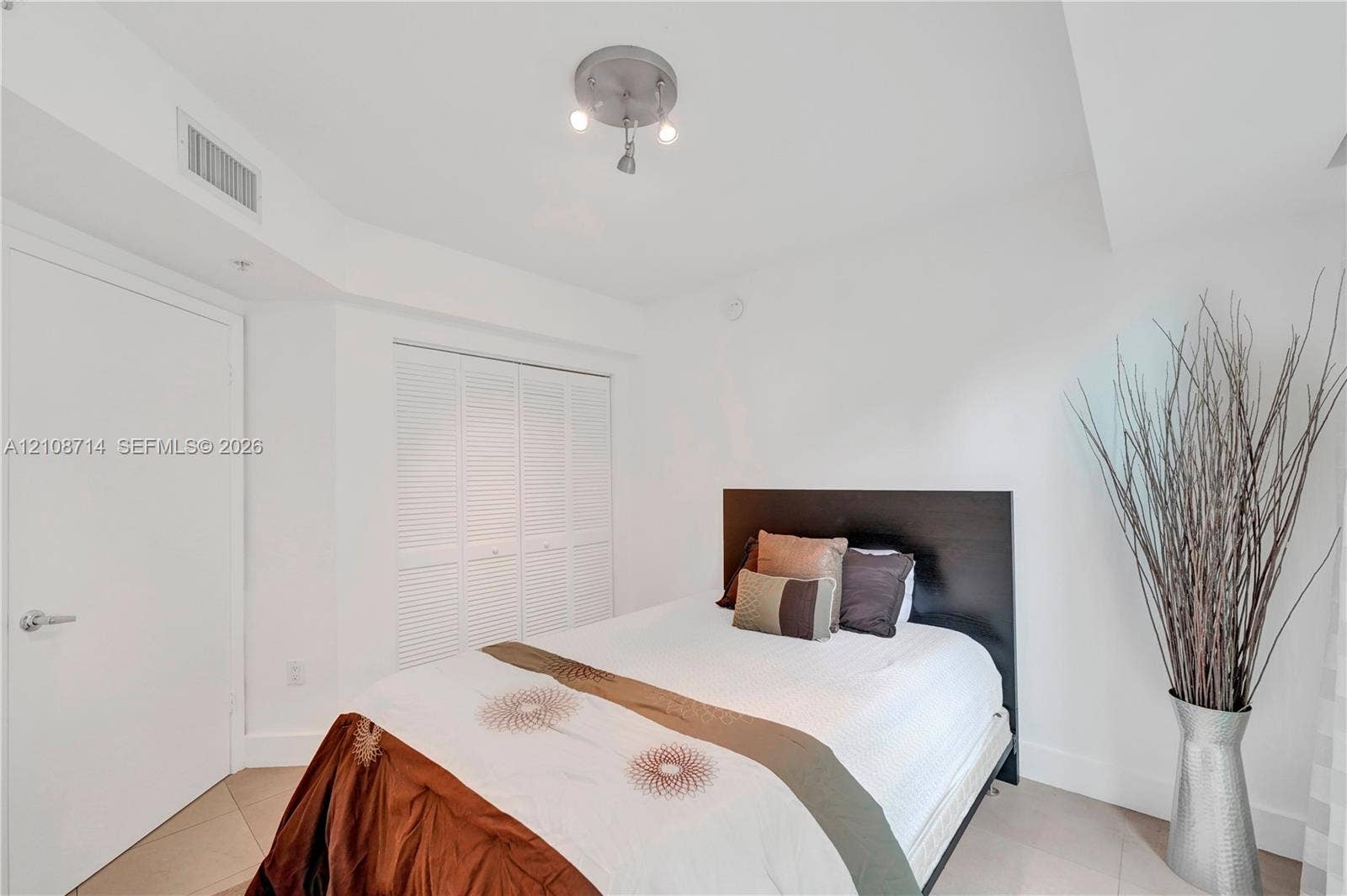 41 SE 5th Street, #317, Miami, Miami, FL 33131 Neutral-toned interior featuring polished tile flooring, white walls, louvered bi-fold closet doors, and a brushed nickel multi-arm flush-mount ceiling light fixture
