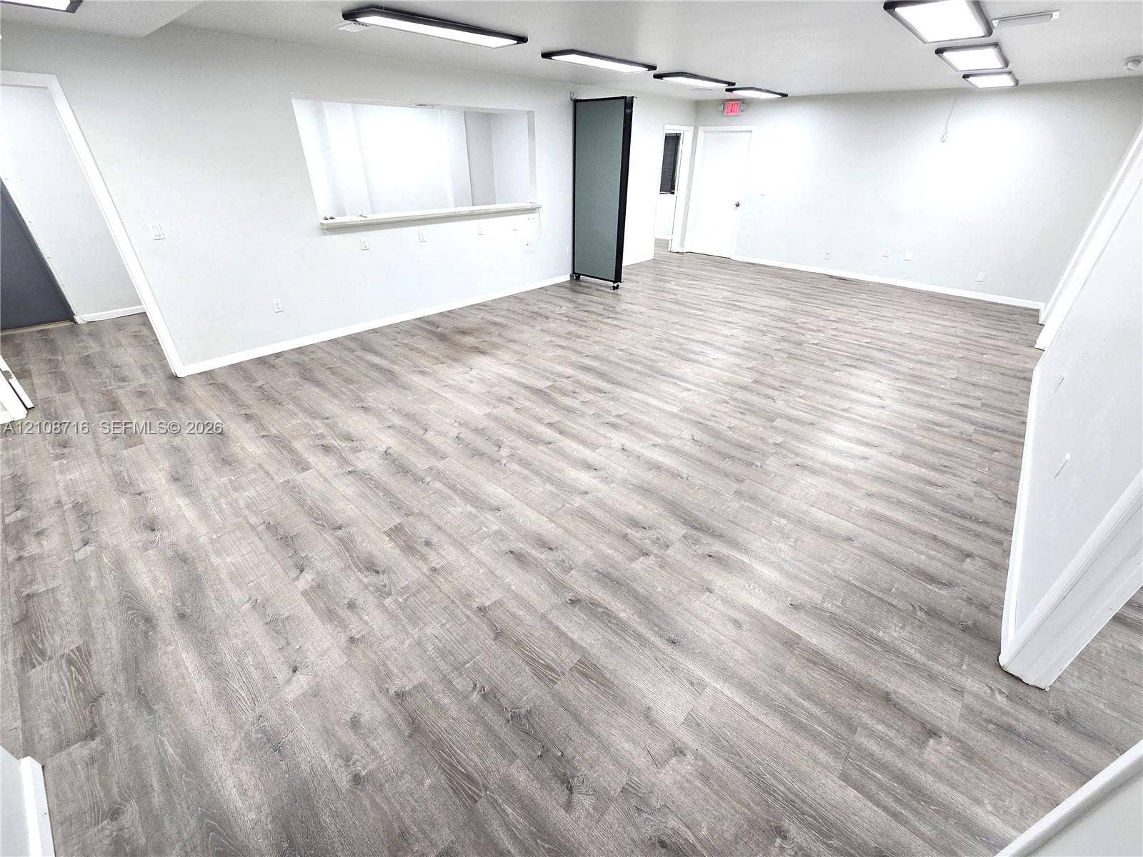 Open-concept interior featuring wood-finish flooring, linear recessed ceiling lighting, and a service pass-through window