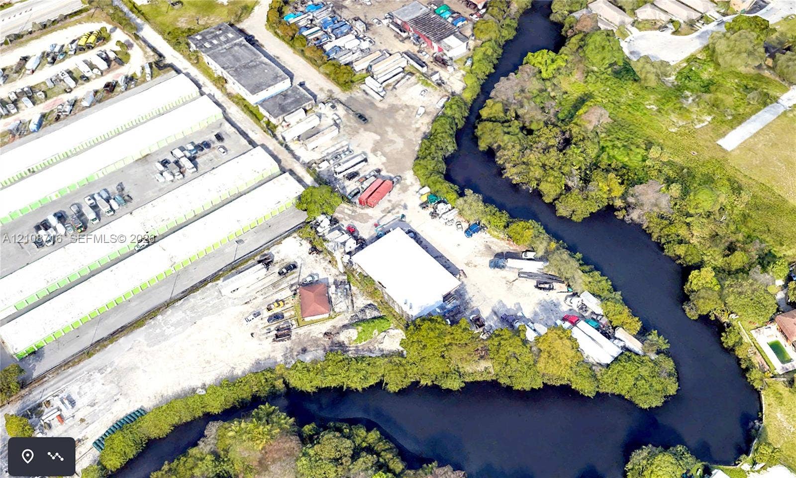 Aerial perspective of a property featuring a warehouse structure, expansive unpaved lot, and direct water frontage